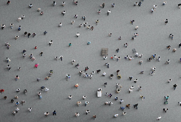 Aerial view of a crowd scattered across a grey plaza, people drifting past each other