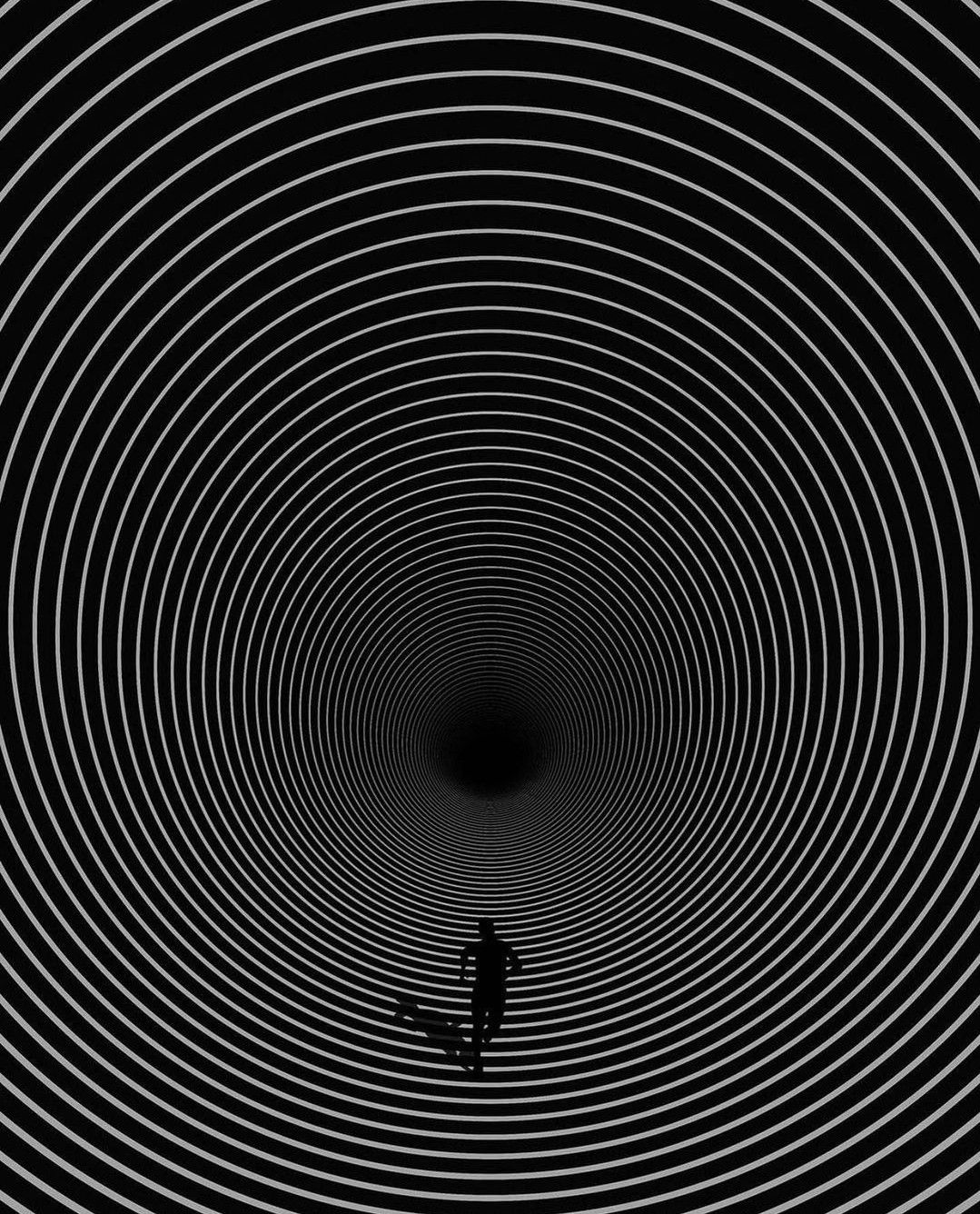 A tiny figure falling into a vortex of concentric white rings on black