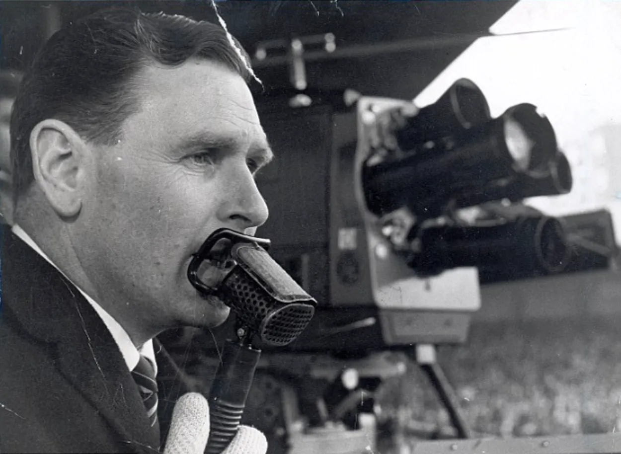 Close-up of commentator speaking into microphone, old broadcast camera behind