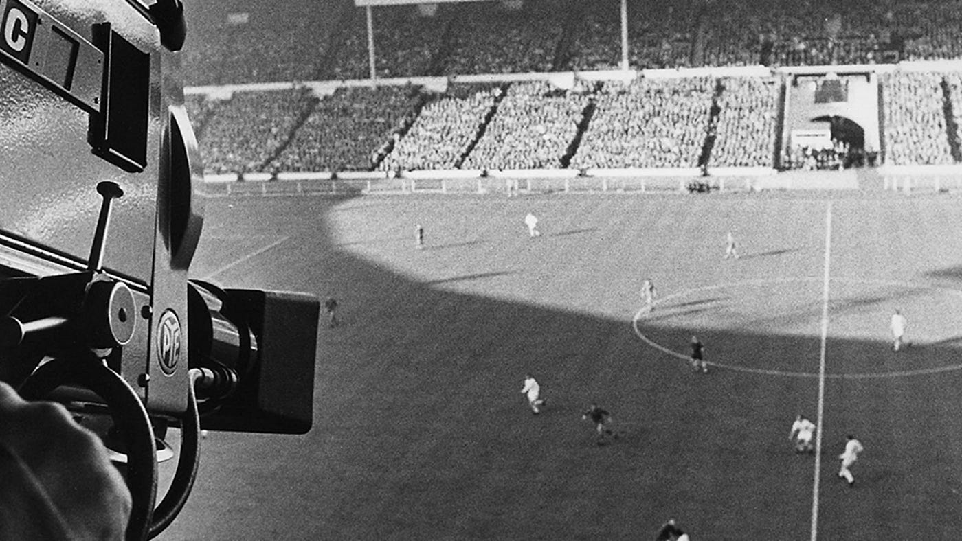 Film-era TV camera in foreground, aerial stadium shot behind