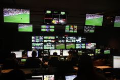 Dark broadcast gallery — operators at desks, banks of football match feeds