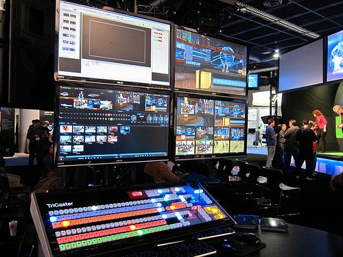 TriCaster production switcher desk with multi-monitor studio feed wall behind