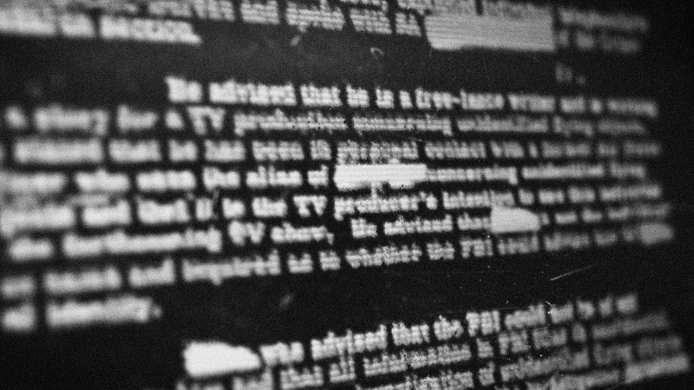 Out-of-focus typewritten document with redaction bars over the text